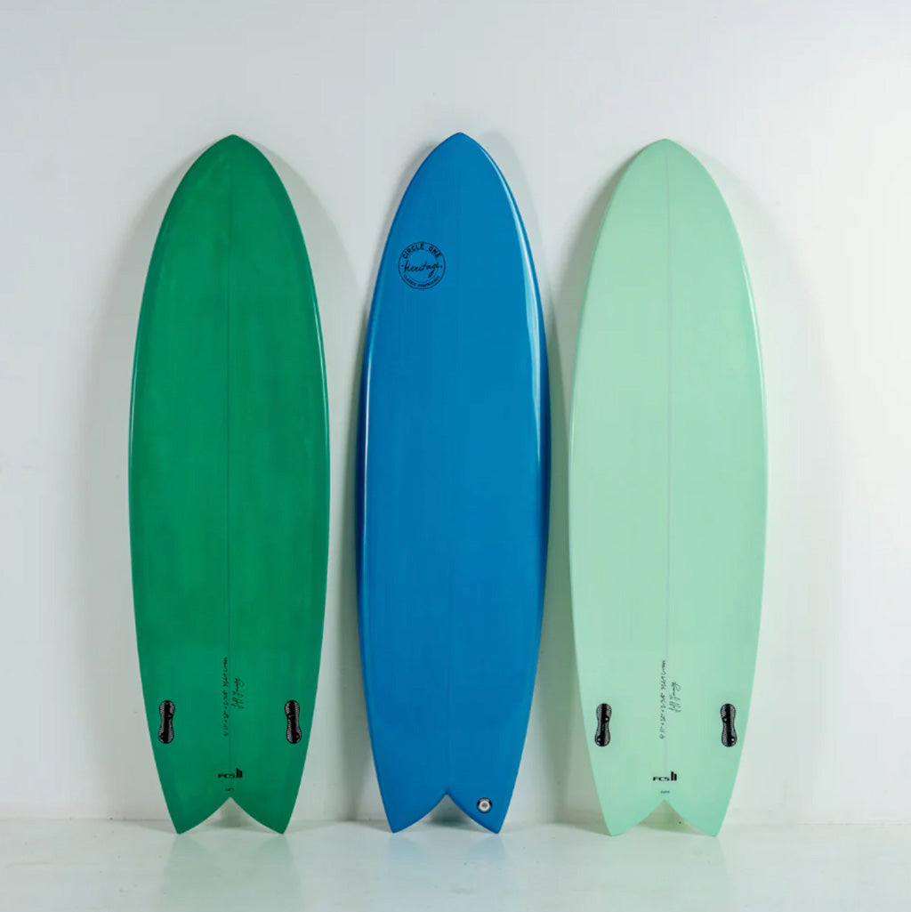Circle One Heritage Fish standing upright against a plain white wall: one green, one blue, and one pale mint green, shown from the bottom side with fins and tail hardware visible.