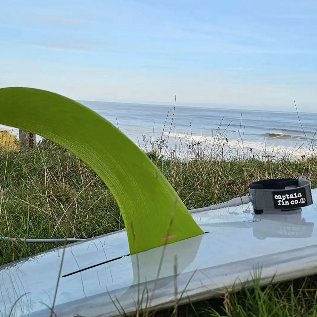 Surfboard with a green fin and 'captain fin co.' logo on a grassy beach.