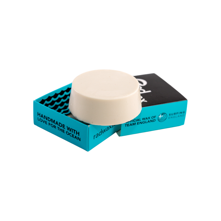 A round cream-colored wax melt or soap block displayed on top of its packaging, which consists of a turquoise and black cardboard box with white text, set against a plain white background.