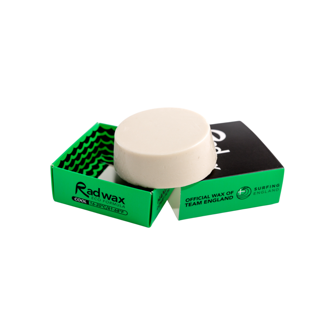 A round off-white wax bar sits on top of an open bright green Radwax box, with a second black-and-green Radwax box behind it on a plain white background.