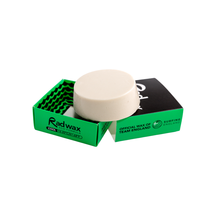 A round off-white wax bar sits on top of an open bright green Radwax box, with a second black-and-green Radwax box behind it on a plain white background.