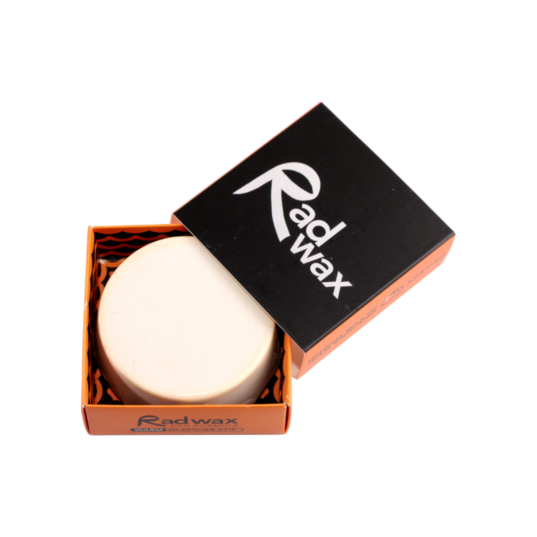 A round white bar of Radwax body wax displayed in its orange cardboard box with a black lid featuring the white Radwax logo, set against a plain white background.