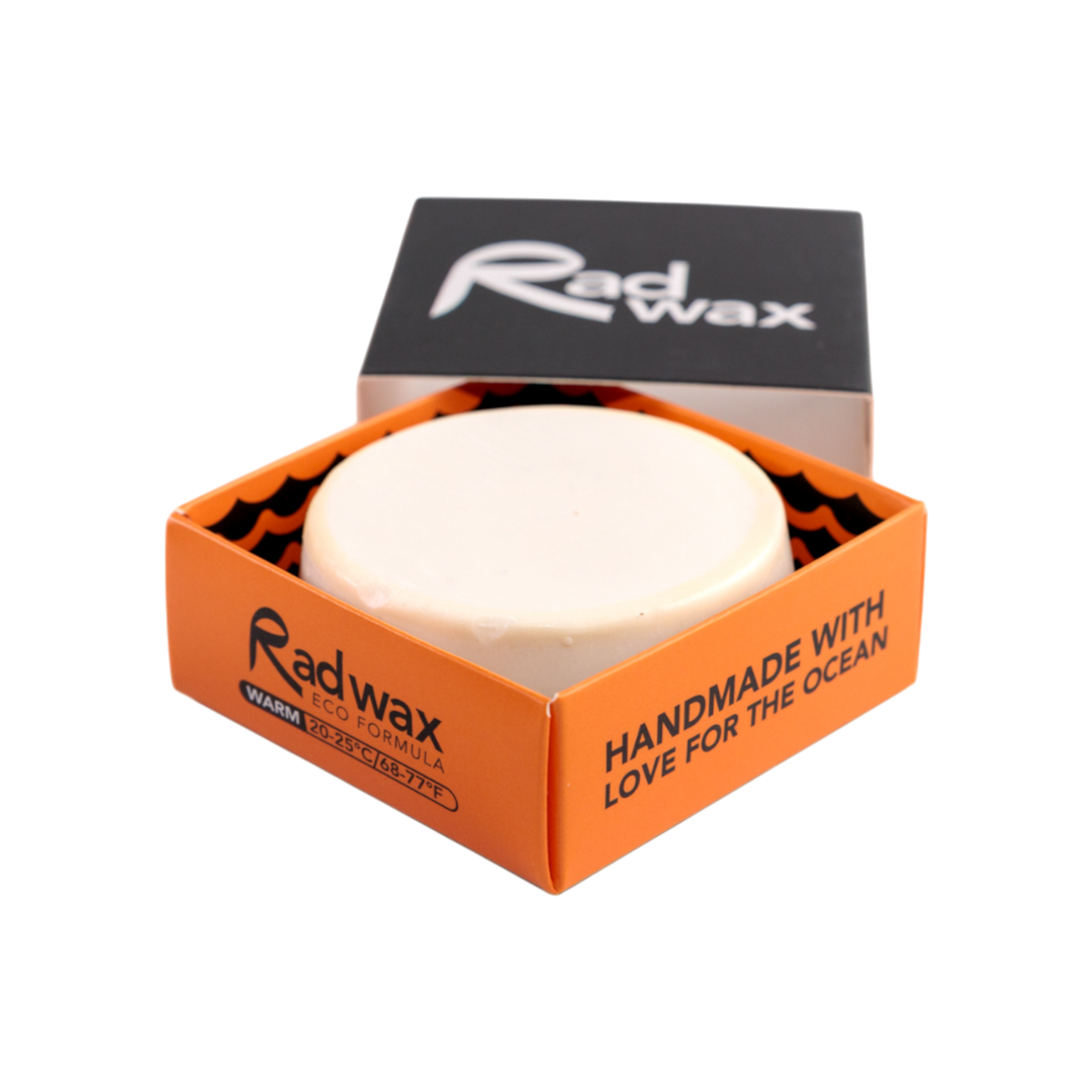A round white bar of Radwax body formula shown in an open orange and black cardboard box with the lid leaning behind it on a white background.