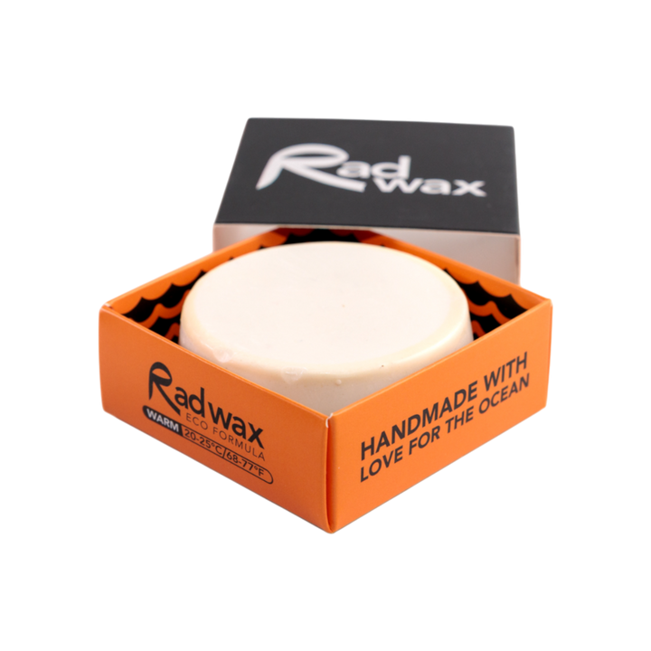 A round white bar of Radwax body formula shown in an open orange and black cardboard box with the lid leaning behind it on a white background.